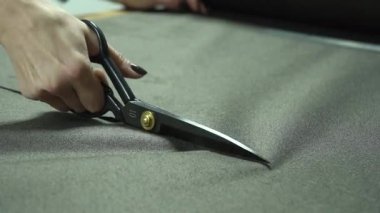 Yoğun bir atölye ortamında gri kumaşı kesen makasın detaylı bir yakın çekimi.