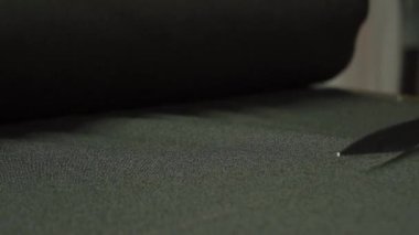 Tecrübeli ve yetenekli bir el, tekstil yüzeyinde kesin bir makas kullanarak koyu bir kumaşı dikkatlice keser.