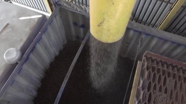 Hava görüntüsü, çeşitli maddelerin endüstriyel bir tesisteki bir konteynıra etkili bir şekilde taşındığını gösteriyor.