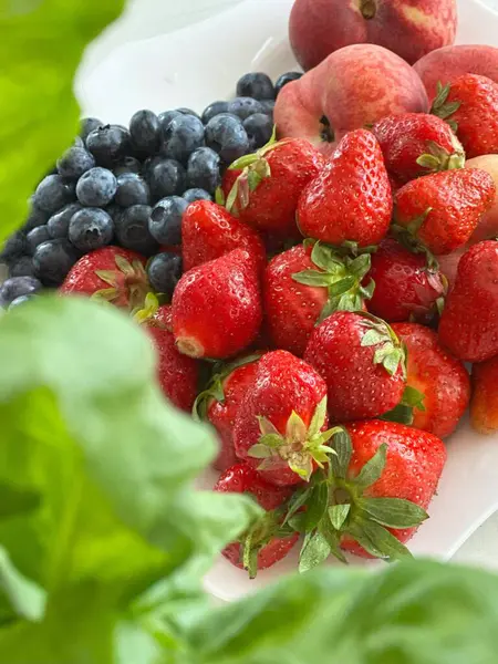 Çilekler, yabanmersinleri ve taze yeşillikler arasında sıralanmış şeftalilerin yer aldığı hoş ve renkli bir vitrin.