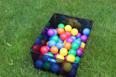 Çimenlikteki bir kutunun içinde bir sürü renk topu var.