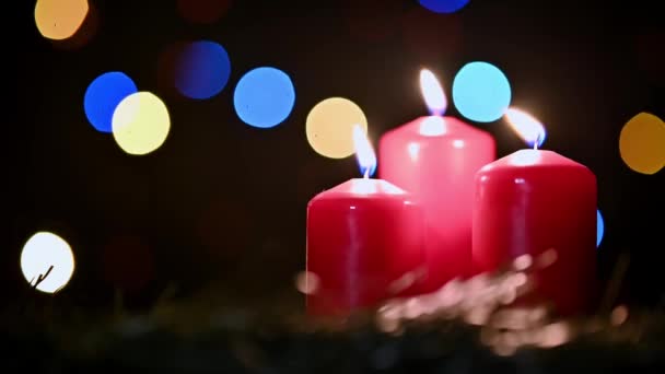 Drie Rode Kaarsen Branden Langzaam Tegen Achtergrond Van Kerstverlichting — Stockvideo