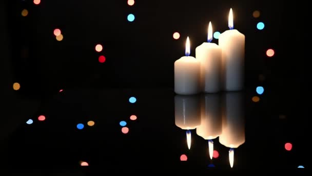 Three Burning Candles Surface Dark Mirror Blurred Blinking Garlands Background — Stock Video