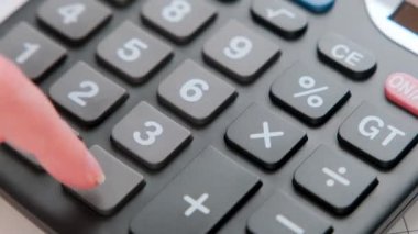 Aylık banka ödemeleriyle ilgili bir hesap makinesinde ev giderlerini hesaplayan bir kadının el resmi..
