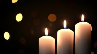 Üç yanan mum, yanıp sönen çelengin arka planında. Mumlar yanar ve bir süre sonra bir rüzgar alevi söndürür.