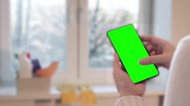 Bulanık pencere ve deterjanın arka planına karşı temizleme servisini kullanan kadın aramaları. Yeşil ekranlı akıllı telefon