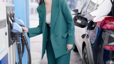 İş kadını benzin istasyonunda arabaya yakıt ikmali yapıyor. Bir kadın yakıt enjektörü kullanarak dizel motoru benzinle dolduruyor..