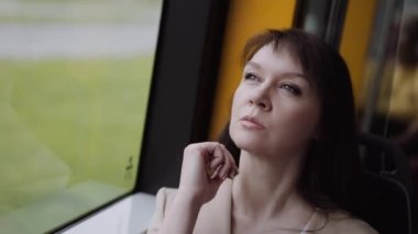 Bir kadın trende ya da otobüste otururken pencereden dışarı bakar..
