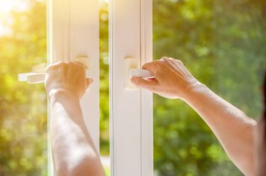 Güneşli bir bahar gününde eller beyaz plastik bir PVC penceresi açar.