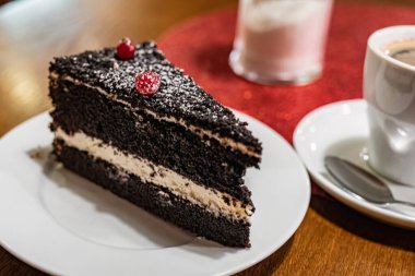 Plate with a slice of delicious homemade chocolate cake and a cup of coffee on the table