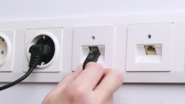 Close-up of a woman's hands inserting an ethernet plug into an internet socket.