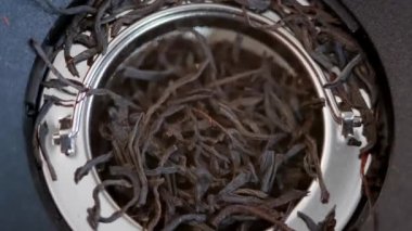 Falling dried green tea leaves into a teapot. Large leaf black tea in glass jar.