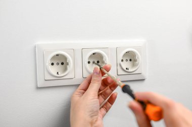 a woman repairs an electrical outlet with a screwdriver. Installing a new outlet in the wall