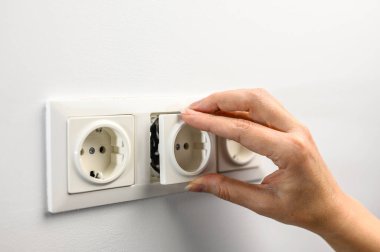 Installing a white AC wall socket with a screwdriver on a white wall, home renovation.
