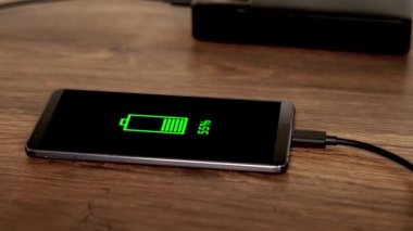 Telefon bir elektrik bankasından şarj oluyor, tahtadan bir masada,% 55 şarj oluyor.