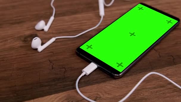 带有空白绿色屏幕和耳机的智能手机放在桌上 用于听音乐的移动应用程序 — 图库视频影像