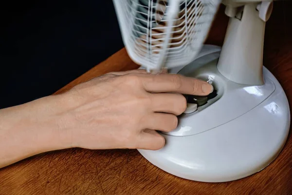 close-up of a person using a household fan. a female hand regulates the temperature of an electric fan.
