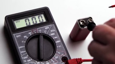 Bataryayı 9 volt için kontrol ediyorum. El, bir çoklu metre ve dokuz voltluk bataryanın sondalarını tutar..