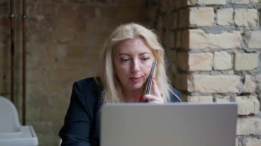 Dizüstü bilgisayarın önünde oturan bir kadın kafede cep telefonuyla konuşuyor..