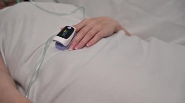Elinde nabız oksimetresi olan bir kadın hasta hastane odasında yatıyor..