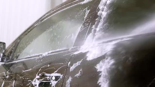 一名工人在洗车时清洗一辆黑色汽车 用白色肥皂 泡沫在车体上手工洗车 — 图库视频影像