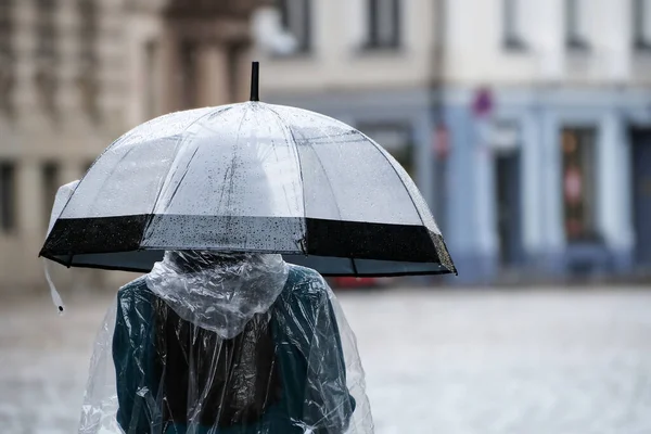 一个女人带着一把透明的雨伞沿着城市街道走着 恶劣天气 — 图库照片