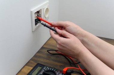 Bir elektrik teknisyeni voltajı çoklu metre test cihazı kullanarak ölçer. Prizdeki voltajı ölçmek.