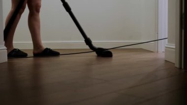 Terlikli ev hanımı, minimalist parlak bir dairede, modern bir elektrikli süpürgeyle katları temizliyor.