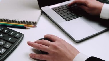 Bir iş adamının hesap makinesi, defter ve kalemlerle bilgisayarı kullanarak ofis işlerini ve finansal görevleri ön plana çıkardığı yakın plan..