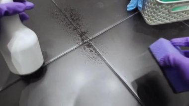 Siyah fayansları temizlerken mor eldiven giyen bir insanın yakın plan fotoğrafı. Sprey şişesi ve bez kullanarak, hijyen ve ev bakımını vurgulayarak..
