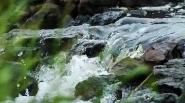 Engebeli karanlık kayaların üzerinden akan tatlı suyun sakin doğal akış ortamında yakın plan görüntüsü.