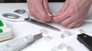 Beyaz masadaki ethernet kablolarını kesen ellerin yakın çekimi ve etrafa saçılmış ağ araçları.