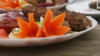 Lezzetli ızgara et ve taze sebze garnitürü. Sıcak bir yemek ortamında beyaz bir tabakta servis ediliyor.