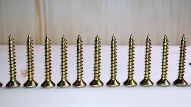 Altın metal vidaların yakın çekim görüntüsü bir atölyede ahşap bir yüzey üzerinde düzgünce dizilmişti.