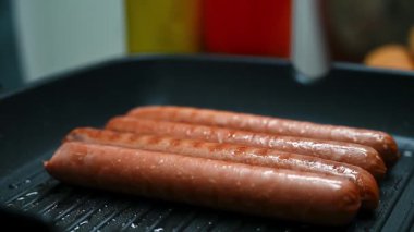 Sulu sosisli sandviçlerin yakın plan çekimi. Ev yemeği ortamında soba tepsisi ve siyah mutfak maşasıyla ızgara yapıyorlar.