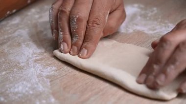 Sıcak bir mutfak ortamında unlu ahşap bir yüzey üzerinde ustalıkla hamur şekillendiren eller yakın plan.
