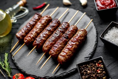 Baharatlı ve otlu ızgara sosisler ve siyah taş arka planda.