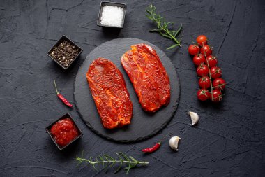 Baharatlı çiğ biftek ve siyah arka planda otlar.