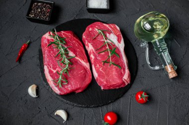 Baharatlı çiğ biftek ve siyah arka planda otlar.