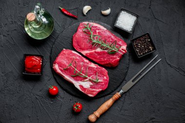 Baharatlı çiğ biftek ve siyah arka planda otlar.