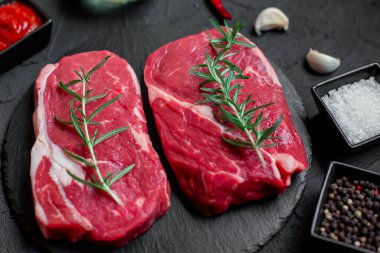 Baharatlı çiğ biftek ve siyah arka planda otlar.