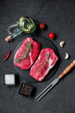 Baharatlı çiğ biftek ve siyah arka planda otlar.