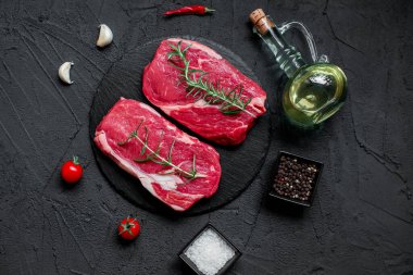 Baharatlı çiğ biftek ve siyah arka planda otlar.