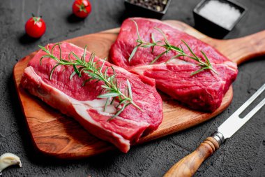 Baharatlı çiğ biftek ve siyah arka planda otlar.