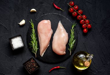 Baharatlı çiğ tavuk göğsü, otlar ve siyah arka planda sebzeler