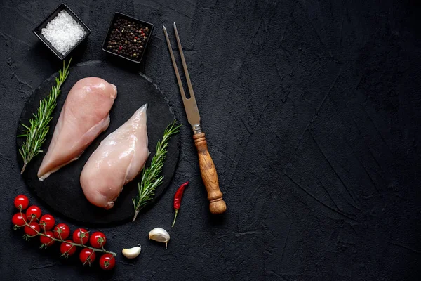 stock image raw chicken breasts with spices, herbs and vegetables on black background with copy space