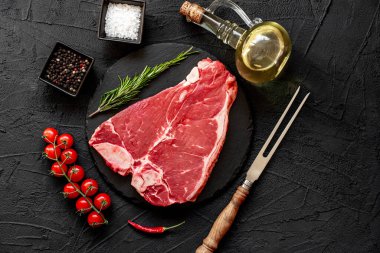 Baharatlı çiğ biftek ve siyah arka planda otlar.