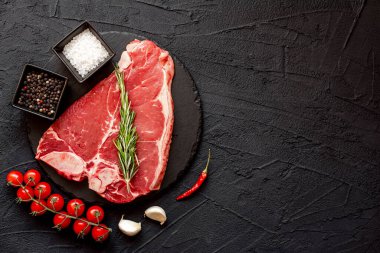 Baharatlı çiğ biftek ve siyah arka planda otlar.