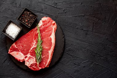 Baharatlı çiğ biftek ve siyah arka planda otlar.