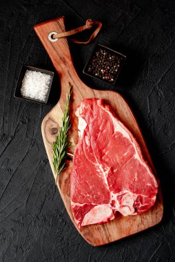 Baharatlı çiğ biftek ve siyah arka planda otlar.